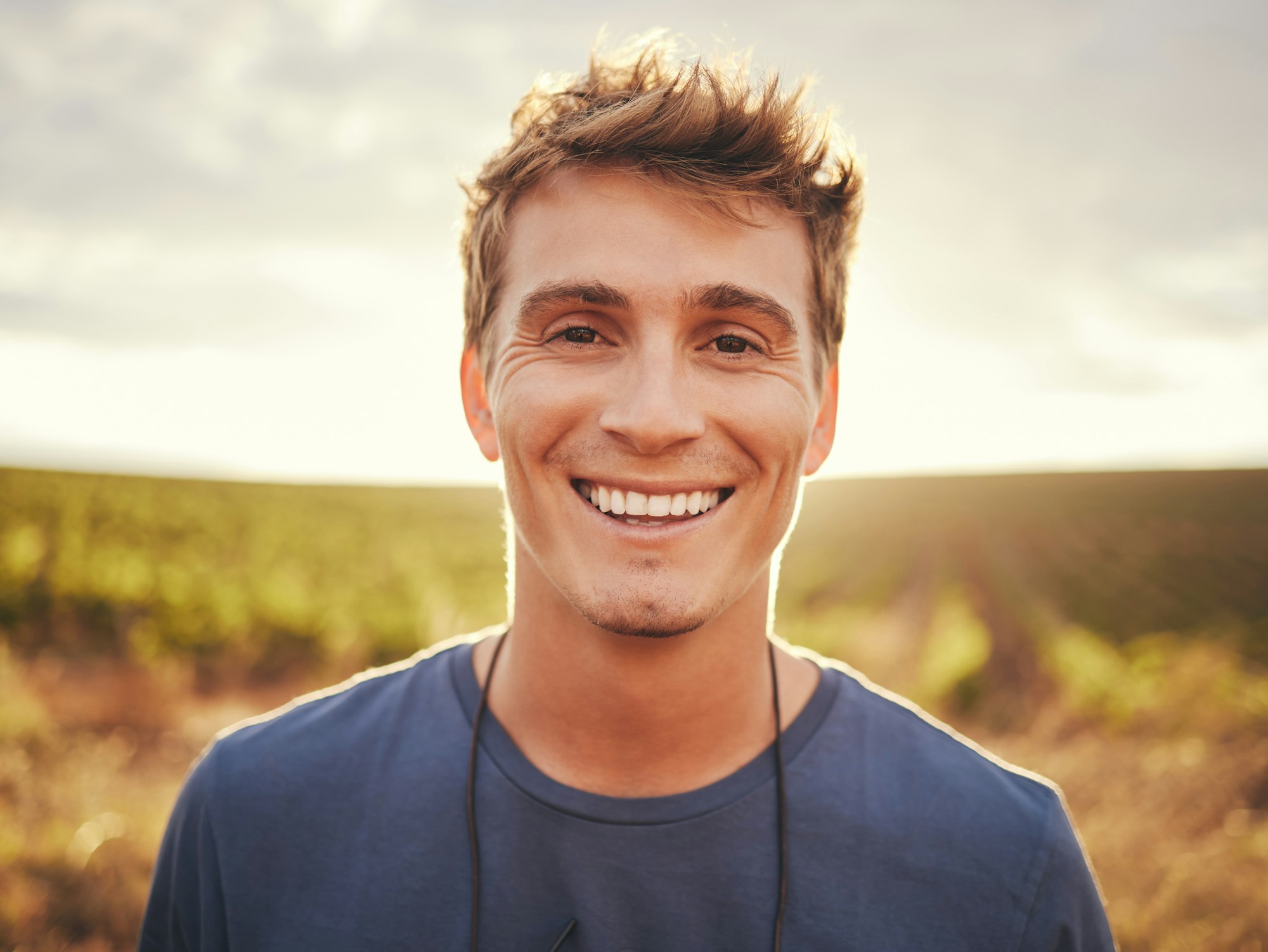 Happy, face and nature with a man at sunset, enjoying freedom with a smile and standing on a field