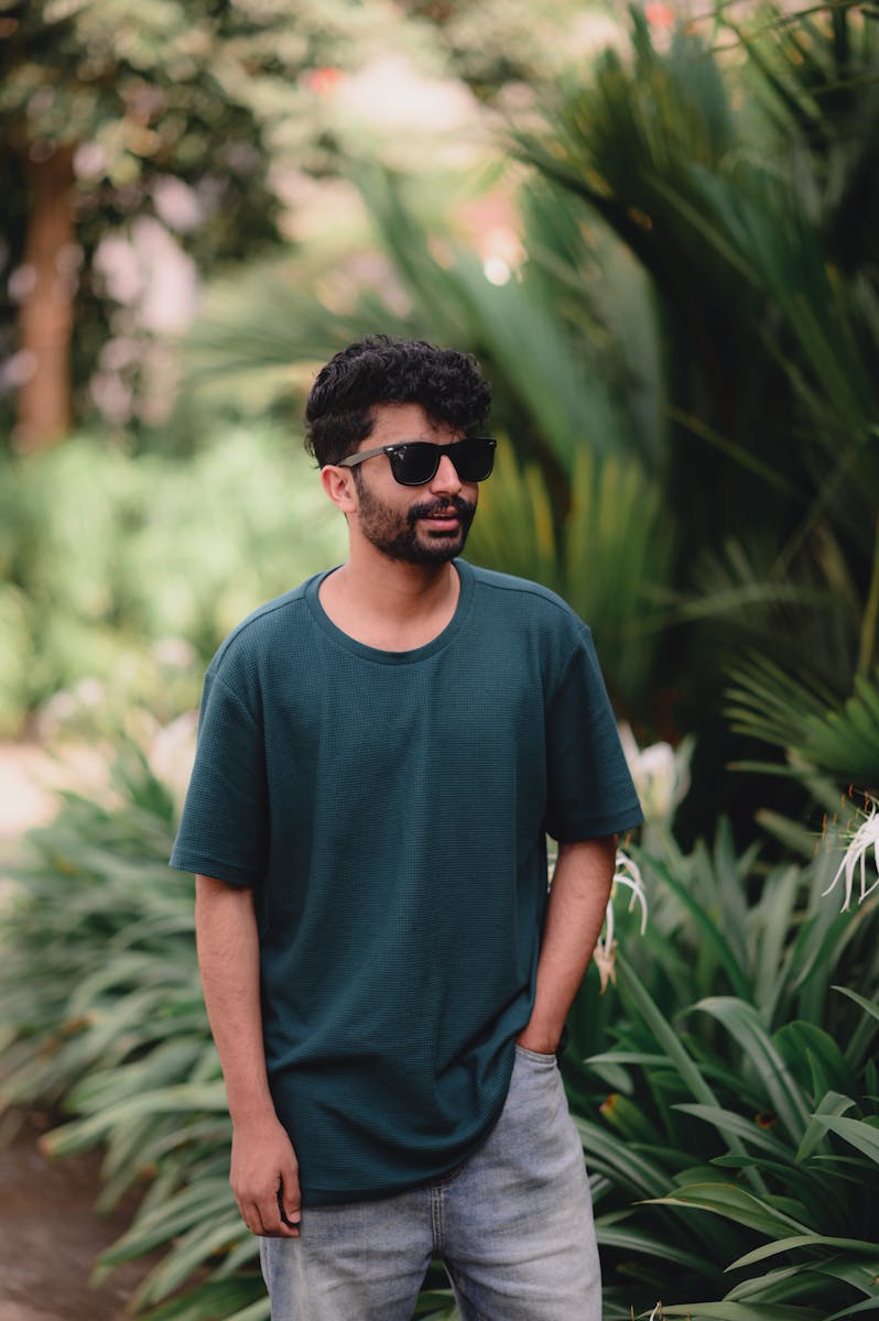 Young Man in a Casual Outfit and Sunglasses Standing near Green Plants